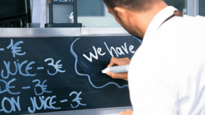 A food truck owner writing on a chalkboard who understands that securing food truck financing options to purchase the truck and cover other associated costs is important when starting a food truck business.